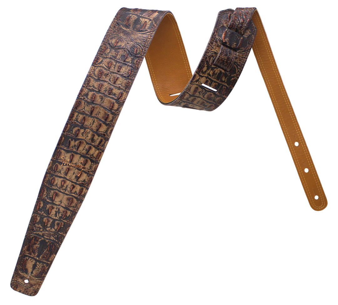 A brown leather guitar strap featuring a textured alligator or crocodile pattern on one side and smooth tan leather on the reverse, displayed against a white background.